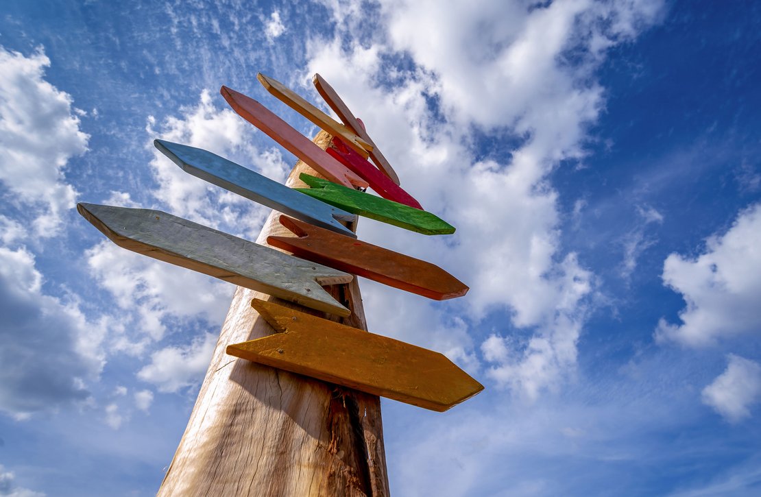 alt= "Ein bunter Wegweiser aus Holz, der unbeschriftet ist."
